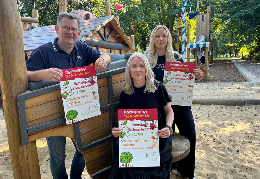 3 Personen werben auf einem Spielplatz für den Tag der offenen Tür in der Kindertagespflege